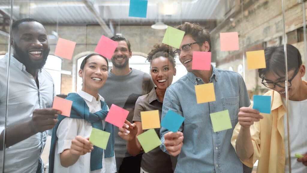 des collegues souriant collent des post it sur un mur de verre